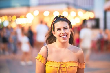 Genç ve güzel bir kız mutlu ve kendinden emin gülümsüyor. Gece lambalarının etrafında yüzünde bir gülümsemeyle, kasaba sokaklarında yürüyor.