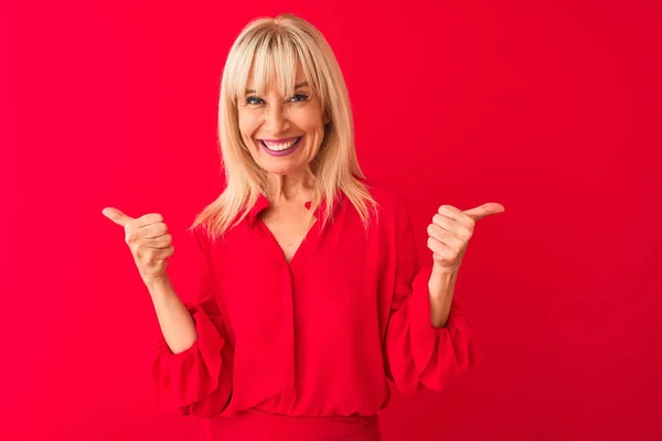 中年妇女穿着雅致的衬衫站在孤立的红色背景的成功标志上 手拿着积极的手势 竖起大拇指 微笑着 快乐地 快乐的表情和胜利的姿态 — 图库照片