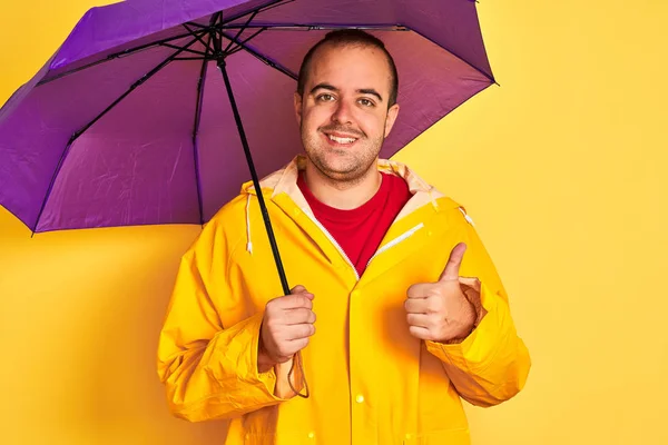 Mor Şemsiyeli Yağmurluk Giyen Genç Adam Izole Edilmiş Sarı Arka — Stok fotoğraf