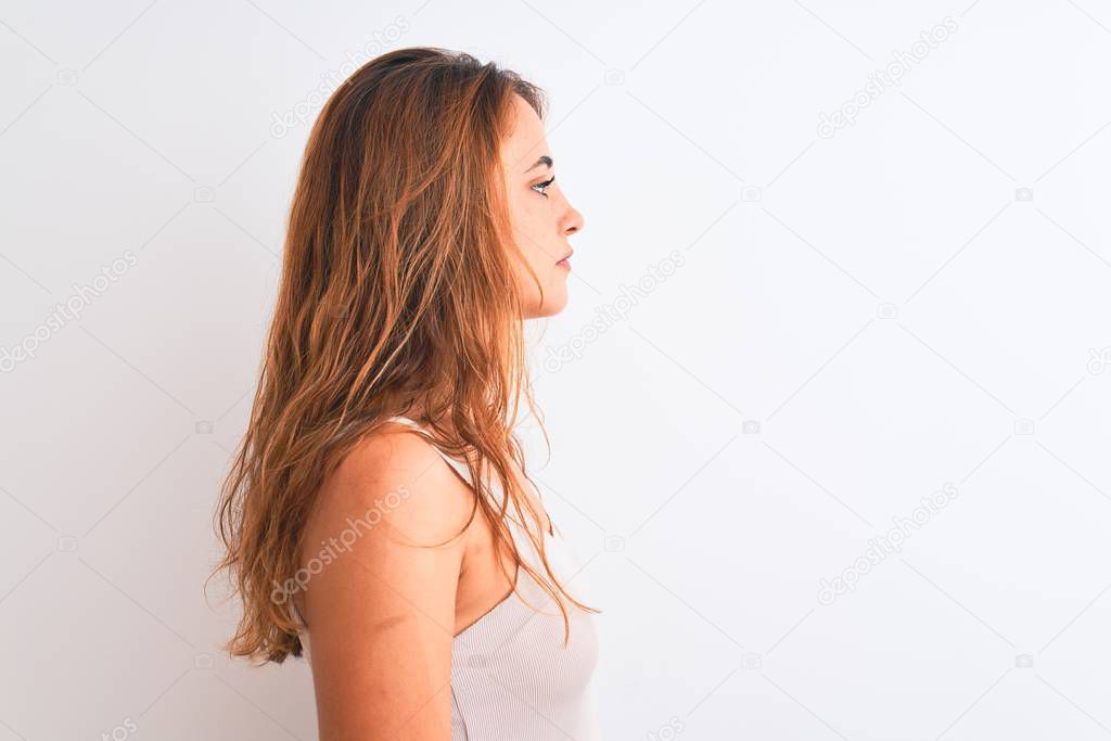 Young redhead woman wearing casual t-shirt stading over white isolated background looking to side, relax profile pose with natural face with confident smile.