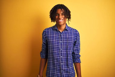 Rastgele tişörtlü Afro bir adam izole edilmiş sarı arka planda mutlu ve havalı bir gülümsemeyle dikiliyor. Şanslı kişi..