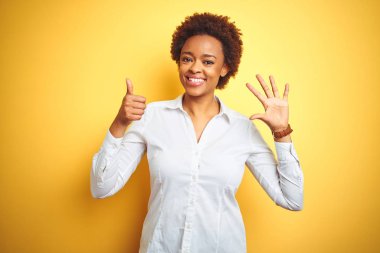 Afro-Amerikalı iş kadını, izole edilmiş sarı arka planda altı numarayı gösterip işaret ederken kendinden emin ve mutlu gülümsüyor..