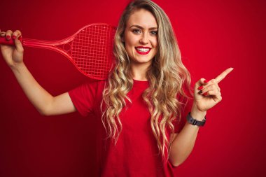 Genç sporcu raketle tenis oynuyor ve kırmızı izole bir zemin üzerinde bir top çok mutlu bir şekilde el ve parmak kenarı işaret ediyor.