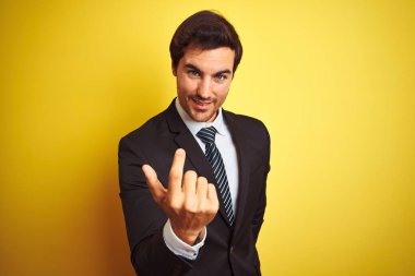 Takım elbiseli ve kravatlı yakışıklı genç bir işadamı izole edilmiş sarı arka planda duruyor.