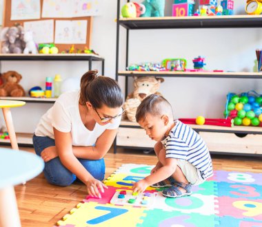 Güzel öğretmen ve küçük çocuk bulmacanın üzerinde oturup anaokulunda rakamlarla oynuyorlar.