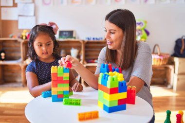 Güzel öğretmen ve küçük kız anaokulunda inşaat bloklarıyla oynuyorlar.