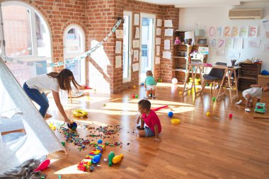 Anaokulunda bir sürü oyuncağın etrafında basketbol oynayan genç ve güzel öğretmenler ve yeni yürümeye başlayan çocuklar.