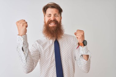 Genç kızıl saçlı İrlandalı işadamı, izole edilmiş beyaz arka planda durup kolları havada ve gözleri kapalı bir şekilde başarının şaşkınlığını ve şaşkınlığını kutluyor. Kazanan konsept.