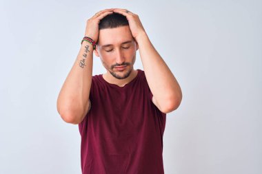 Genç yakışıklı adam izole edilmiş arka planda duruyor. Baş ağrısı, çaresiz ve stresli. Çünkü acı ve migren. Ellerini başının üstüne koy..
