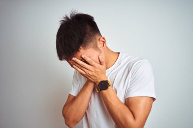 Asyalı genç bir Çinli tişört giyiyor. İzole edilmiş beyaz arka plan üzerinde duruyor. Üzücü bir yüz ifadesi var. Depresyon kavramı.