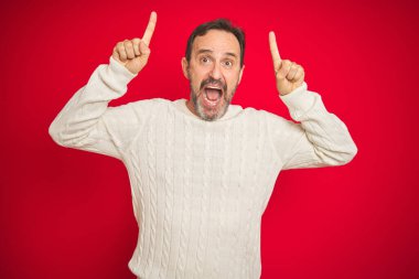 Yakışıklı orta yaşlı, gri saçlı, soyutlanmış kırmızı arka planı olan, şaşkın, şaşkın, parmaklarıyla işaret eden ve kollarını kaldıran yaşlı bir adam..