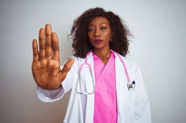 İzole edilmiş beyaz arka plan üzerinde pembe steteskop takan Afrikalı Amerikalı doktor kadın avucunun içi gibi şarkı söylemeyi kesiyor. Yüzünde olumsuz ve ciddi bir jest olan uyarı ifadesi.