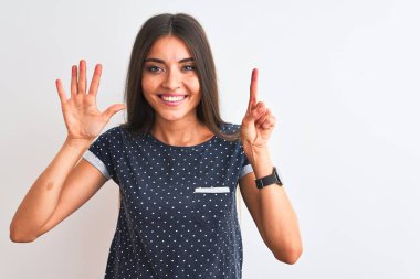 Mavi günlük tişört giyen genç güzel bir kadın izole edilmiş beyaz arka plan üzerinde duruyor ve altı numaralı parmaklarıyla işaret ederken kendinden emin ve mutlu gülümsüyor..