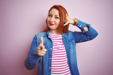 Güzel kızıl saçlı kadın kot gömlek ve çizgili tişört giyiyor pembe arka planda gülümsüyor telefonda konuşuyor ve seni işaret ediyor. Ara beni..