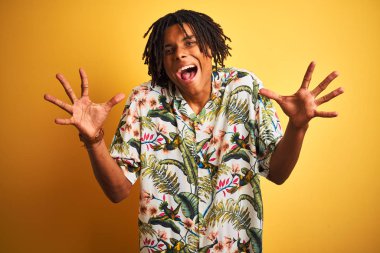 Tatilde rastalı bir afro adam sarı arka planda, izole edilmiş bir tişört giyiyor çılgın ve başarısını kutluyor. Kolları havada ve gözleri açık, heyecanlı bir şekilde çığlık atıyor. Kazanan konsept