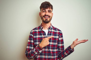 İzole edilmiş beyaz arka plan üzerinde duran gündelik gömlekli genç adam hayrete düşmüş ve kameraya gülümserken eliyle ve parmağıyla işaret ediyordu..