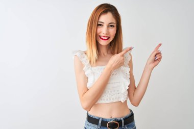 İzole beyaz arka plan üzerinde ayakta rahat t-shirt giyen güzel Redhead kadın gülümseyen ve yan iki el ve parmak ile işaret kamera bakıyor.