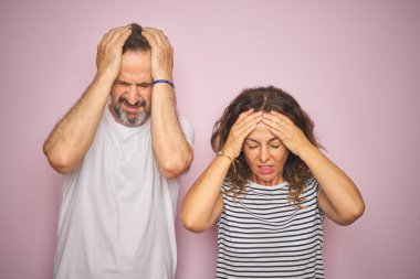 Güzel orta yaşlı bir çift baş ağrısı ve stresten muzdarip pembe arka planda dikiliyorlar. Çünkü acı ve migren. Ellerini başının üstüne koy..