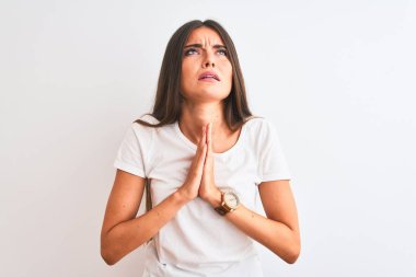 Genç güzel kadın rahat t-shirt izole beyaz arka plan üzerinde ayakta yalvarıyor ve elleri ile birlikte umut ifadesi ile dua yüz çok duygusal ve endişeli. Af dilemek istiyorum. Din kavramı.