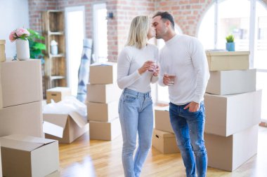 Genç ve güzel bir çift ayakta kahve içiyor ve yeni evlerinde karton kutuların etrafında öpüşüyorlar.