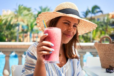 Güzel bir kadın oteldeki barın havuzunda oturmuş yaz tatili için sağlıklı meyve suyu içiyor.