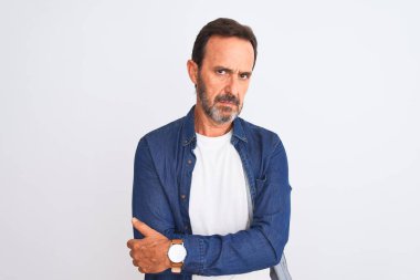 Orta yaşlı, mavi kot gömlek giyen yakışıklı bir adam izole edilmiş beyaz arka plan üzerinde duruyor şüpheci ve gergin, yüzünde çapraz kollu tasvip etmeyen bir ifade. Negatif kişi.