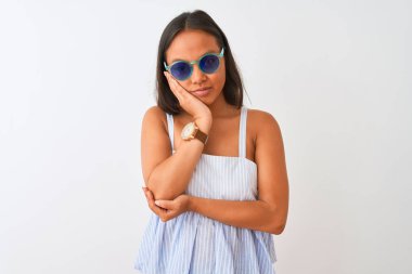 İzole edilmiş beyaz arka plan üzerinde çizgili elbise ve güneş gözlüğü takan genç Çinli kadın çapraz kollu depresyon sorunlarından yorgun ve sıkılmış göründüğünü düşünüyor..