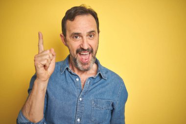 Sarı arka planda gri saçlı yakışıklı orta yaşlı bir adam başarılı bir fikri işaret ediyor. Heyecanlı ve mutlu. Bir numara..