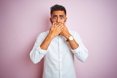 Soyutlanmış pembe arka planda duran zarif gömlekli genç Hintli işadamı yanlışlıkla ağızlarını kapatarak şok geçirdi. Gizli konsept.