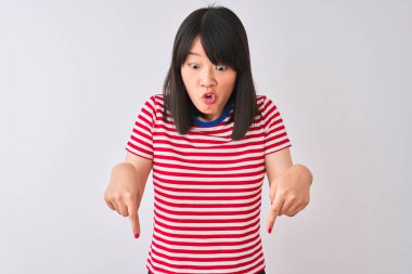 İzole edilmiş beyaz arka plan üzerinde kırmızı çizgili tişört giyen genç, güzel Çinli kadın parmaklarını göstererek reklamını yapıyor, şaşırmış yüzünü ve ağzını açıyor.