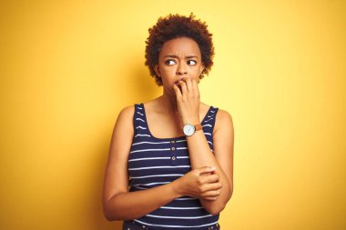 Beauitul afro-amerikan kadın izole sarı arka plan üzerinde yaz t-shirt giyen stresli ve ağız tırnak ısırma elleri ile sinirli görünümlü. Anksiyete sorunu.