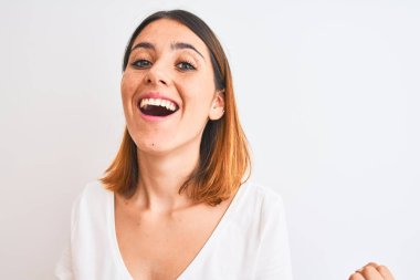 Güzel kızıl saçlı kadın, izole edilmiş arka planda günlük beyaz tişört giyiyor gururla bağırıyor, zaferi kutluyor ve başarıyı kutluyor çok heyecanlı, coşkulu bir duygu.