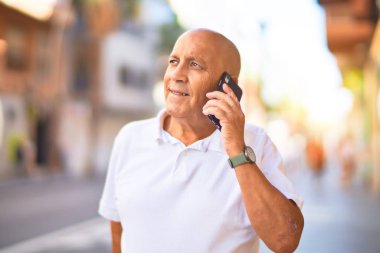 Kıdemli yakışıklı adam mutlu ve kendinden emin gülümsüyor. Yüzünde gülümsemeyle kasaba caddesinde telefonla konuşuyor.
