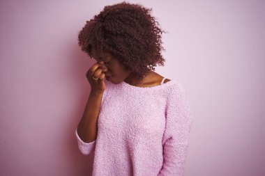 İzole edilmiş pembe arka plan üzerinde dikilen Afrikalı genç bir afro kadın yorgun burnu ve gözleri ovuşturup yorgunluk ve baş ağrısı hissediyor. Stres ve hüsran kavramı.