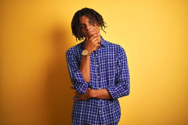 Rastgele tişörtlü Afro bir adam izole edilmiş sarı arka plan üzerinde duruyor kameraya bakıyor kollarını kavuşturup gülümseyerek ve çenesini kaldırarak bakıyor. Olumlu düşünüyorum..