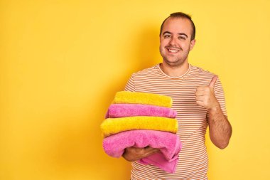 Sarı arka planda duran katlanmış havluları tutan genç bir dükkan sahibi mutlu bir şekilde gülümsüyor.