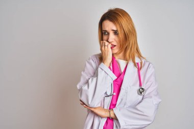İzole edilmiş arka planda pembe steteskop takan kızıl saçlı doktor elleri ağız yiyen tırnaklarla stresli ve gergin görünüyor. Endişe sorunu.