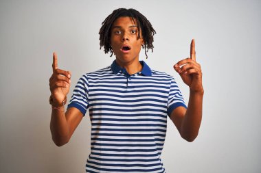 Sarı çizgili mavi polo giyen Afro adam izole edilmiş beyaz arka planda durup hayrete düşmüş ve parmaklarıyla işaret ederek ve kollarını kaldırarak şaşırmıştı..