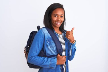 Afrika kökenli Amerikalı genç bir bayan sırt çantası takıyor. Büyük bir gülümsemeyle mutlu. İşaret veriyor, parmaklarıyla başparmağını kaldırıyor.