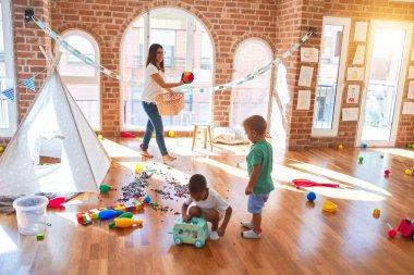 Anaokulunda bir sürü oyuncağın etrafında basketbol oynayan genç ve güzel öğretmenler ve yeni yürümeye başlayan çocuklar.