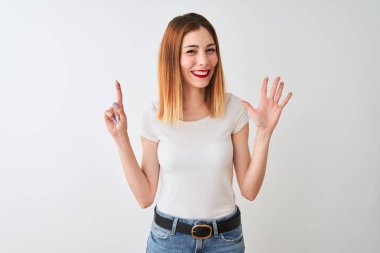 Güzel kızıl saçlı kadın rahat t-shirt izole beyaz arka plan üzerinde duran gösteren ve parmakları ile işaret ederken emin ve mutlu gülümseyerek altı.