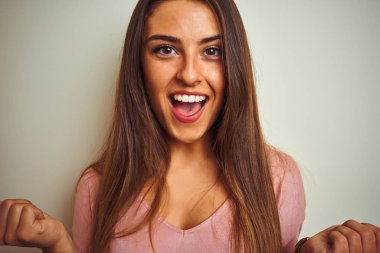 Pembe tişört giyen genç güzel bir kadın izole edilmiş beyaz arka planda durup gururla haykırıyor zaferi ve başarıyı kutluyor çok heyecanlı, coşkulu bir duygu.