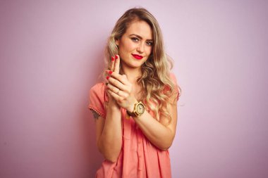 Pembe izole edilmiş arka planda duran tişört giyen genç güzel bir kadın sembolik bir silahla el kol hareketi yapıyor, cinayet silahlarıyla oynuyor, sinirli bir yüz ifadesi takınıyor.