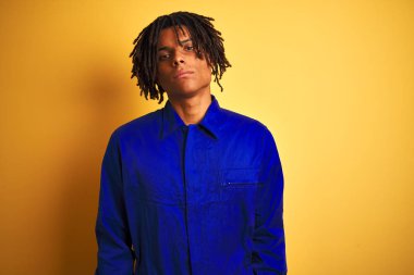 Sarı arka plan üzerinde mekanik üniforma giyen Afrikalı işçi yüzünde ciddi bir ifadeyle rahatlamış. Basit ve doğal bir şekilde kameraya bakıyorsun..