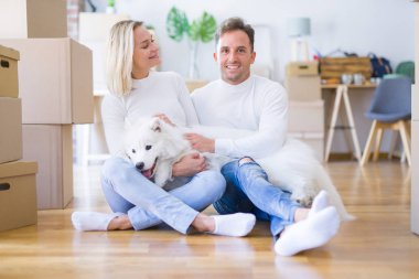 Karton kutular etrafında yeni evde yerde oturan köpek ile genç güzel çift