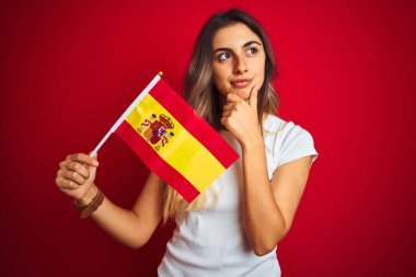 İspanyol bayrağını kırmızı arka planda tutan genç ve güzel bir kadın. Ciddi bir yüz. Soru sormayı düşünüyor.
