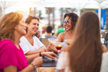 Güzel bir grup kadın restoranın terasında oturmuş kokteyller içiyor konuşuyor ve gülümsüyor.