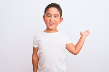 Güzel çocuk, izole edilmiş beyaz arka planda duran sıradan bir tişört giyip neşeli bir şekilde sunum yapıyor ve avuç içi kameraya bakıyor..