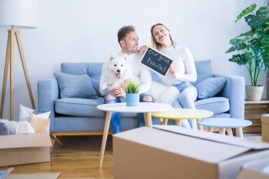 Karton kutular etrafında yeni evde mesaj ile kara tahta tutan kanepede oturan köpek ile genç güzel çift