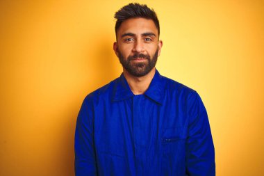 Yüzünde ciddi bir ifadeyle izole edilmiş sarı arka plan üzerinde üniforma giyen yakışıklı Hintli işçi. Basit ve doğal bir şekilde kameraya bakıyorsun..
